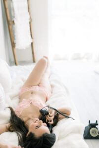 Girl lays on bed while making a call to book her California Boudoir Session with OC Boudoir