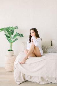 Woman poses snuggled on bed wearing an oversized white shirt as a Boudoir Outfit Ideas