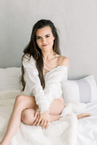 Woman cuddles up on a bed showing what wearing a sweater looks like for a Boudoir Outfit Idea