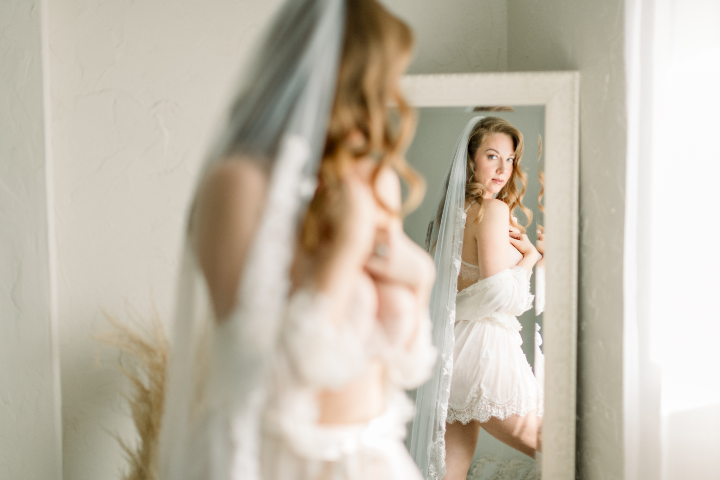 bidal boudoir timeline: A woman wearing a bridal ensemble and looking confidently into the mirror during an elegant bridal boudoir session.
